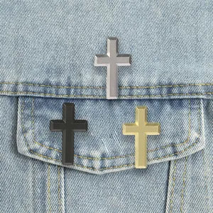 Three beveled metal cross pins in silver, black and gold arranged on a light blue denim pocket.