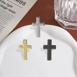Overhead view of three matte metal cross ornaments in silver, gold, and black on a white plate