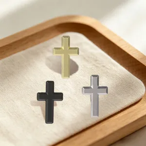 Three small metal cross ornaments in gold, black, and silver arranged on a beige fabric tray