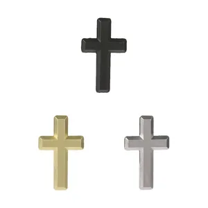 Three matte metal cross brooches in black, gold and silver, arranged on a white background
