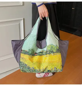 A person holds a roomy tote with a vivid painted field scene, gray side panels, indoors