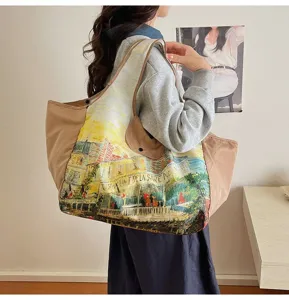 Beige tote worn over the shoulder, with a colorful oil-painted street scene print.