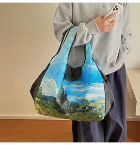 A person carries a large tote with a vivid painted landscape print and black side panels
