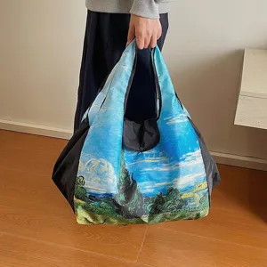 Large foldable nylon shopping tote with a colorful landscape oil painting print, carried by hand