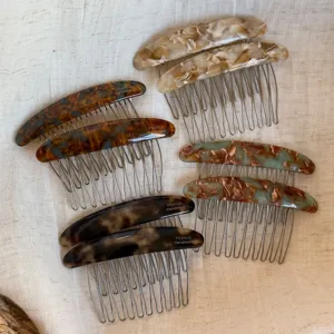 Six marbled resin hair combs with fine metal teeth, arranged on a neutral linen background
