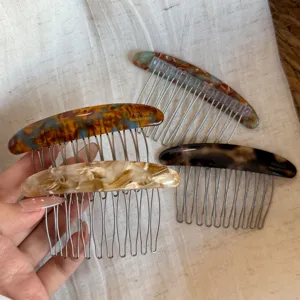 Four curved combs with marbled resin backs and fine metal teeth displayed on neutral linen
