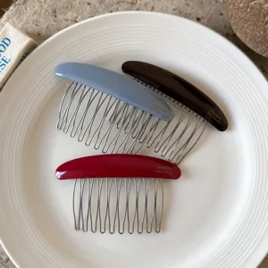 Flat lay of three metal-tooth hair combs with glossy resin backs in mist blue, brown and burgundy