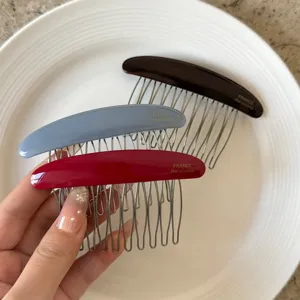 Three curved hair comb clips in brown, mist blue and burgundy, held over a white plate