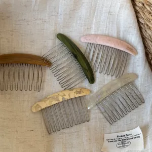 Top view of five curved resin hair combs with metal teeth in brown, green, pink, beige and gray