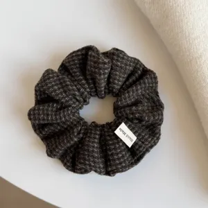Vue rapprochée d’un chouchou tricoté à carreaux brun foncé, à texture douce, avec étiquette handmade