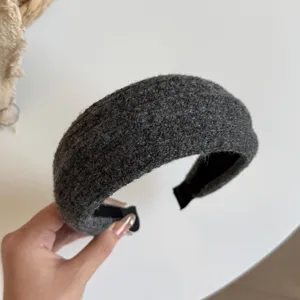 Close-up van een brede donkergrijze haarband met wolachtige textuur, zwarte voering en nette randen.
