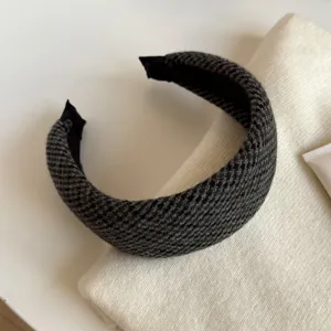 Gros plan sur un serre-tête large en tissu à carreaux gris foncé, doublé de noir, posé sur du tricot