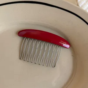 Close-up of a curved red resin comb with slim metal teeth and FRANCE Handmade lettering