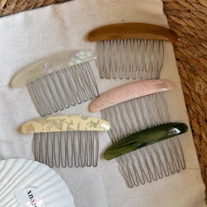 Five resin hair combs in pearl, cream, pink, brown and green, arranged on textured linen