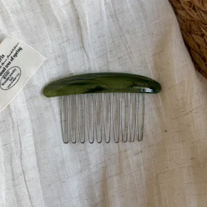 Flat lay showing a curved green marbled comb, silver teeth, and embossed lettering on linen