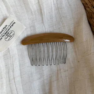 Close-up of a brown resin hair comb with a curved back, silver metal teeth and engraved lettering