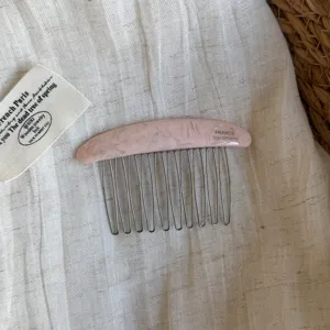 Close-up of a pink marbled hair comb with curved metal teeth, laid on light linen fabric