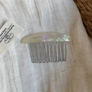 Close-up of an iridescent pearlescent curved comb back with slim metal teeth on linen fabric
