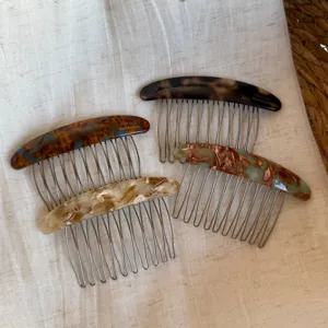 Four French-style hair combs with marbled resin backs and metal teeth arranged on linen fabric