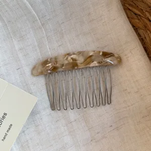 Close-up of a curved comb with mottled brown resin back and slender silver metal teeth