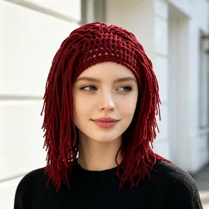 Model wearing a burgundy open-knit cap with long yarn fringe, shown against a bright outdoor wall