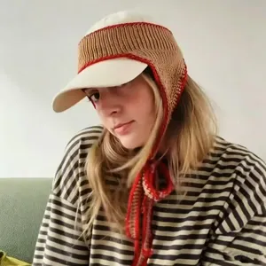 Frau mit gestrickter Ohrenwärmer-Kappe, weißem Schirm, brauner Struktur und roten Bändern