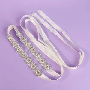 Ivory satin bridal waist belt with sparkling rhinestones and faux pearl floral details, laid flat