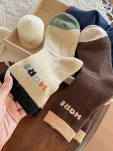 Close-up of color-block knit socks with ribbed cuffs and “MORE” lettering in a cozy display