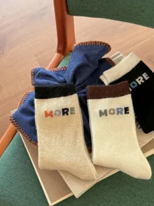 Close-up of beige knit socks with dark ribbed cuffs and colorful MORE lettering on a chair