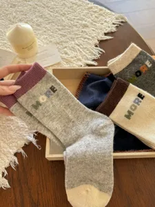 Close-up of knit socks with contrasting ribbed cuffs and MORE lettering in a wooden tray