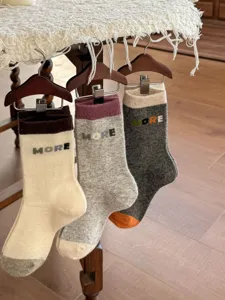 Three pairs of knit socks hang on wooden hangers, showing contrast cuffs, toes and MORE lettering.