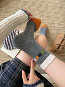 Close-up of a gray knit sock with an orange toe, cream cuff and colorful lettering, worn on foot