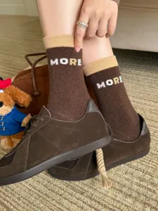 Brown knit socks with camel ribbed cuffs and white “MORE” lettering, worn with casual shoes