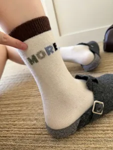 Close-up of a white knit sock with a brown ribbed cuff and colorful lettering, worn with a slipper