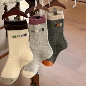 Three pairs of warm mid-calf knit socks in cream and gray, with contrast cuffs and MORE lettering