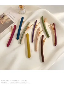 Pinces à cheveux mates de plusieurs couleurs sur soie blanche, près d'un flacon et d'un magazine