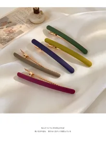 Cinq pinces mates vertes, moutarde, bleu marine, taupe et bordeaux, avec attaches dorées sur satin blanc.
