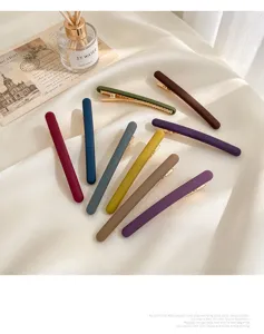 Neuf barrettes mates multicolores avec clips dorés, posées sur un tissu de soie ivoire