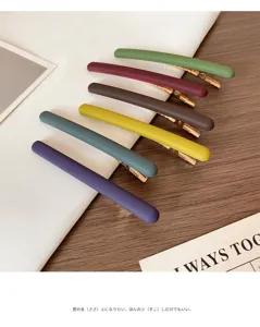 Sept barrettes fines mates, multicolores, avec attaches dorées, disposées en diagonale sur tissu