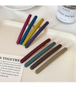Vue de huit barrettes mates colorées avec embouts dorés sur un plateau clair près d'un parfum