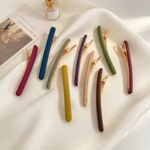 Lot de huit barrettes métalliques mates et colorées, aux dents dorées, posées sur de la soie