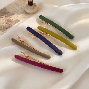 Six barrettes métalliques mates aux couleurs variées, disposées à plat sur du satin blanc