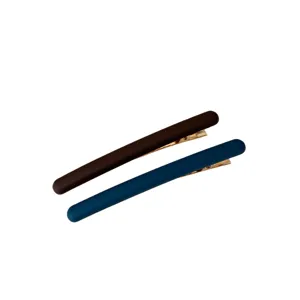 Deux longues barrettes mates, brun foncé et bleu, avec pinces dorées, en diagonale sur fond blanc