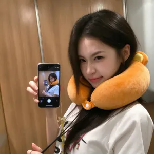 Woman wearing a plush orange U-shaped neck pillow with yellow accents, shown in a mirror selfie
