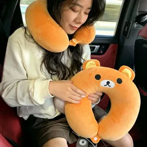 A woman wears an orange bear-shaped neck pillow and holds a matching plush cushion inside a car