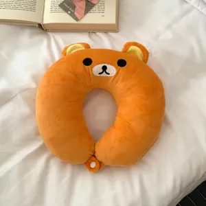 Orange plush bear-shaped neck pillow laid flat on white bedding, with a small clasp at the ends