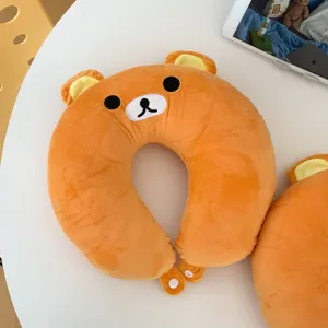 Close-up of the orange plush bear neck pillow, showing its embroidered face and snap fasteners