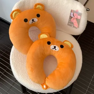 Two orange plush bear-face neck cushions stacked on a white chair, showing embroidered details