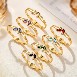 Seven gold-tone hinged bangles with colorful marquise stones and tiny accents on a cream surface