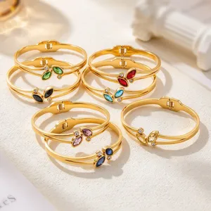 Several gold-tone bangles with colorful marquise-cut stones arranged on a pale textured display